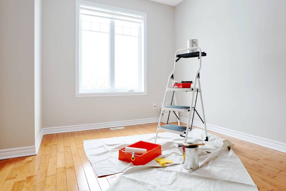 Habitación blanca con una escalera y herramientas de pintura