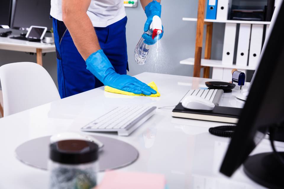Persona limpia una mesa de oficinas con guantes y difusor